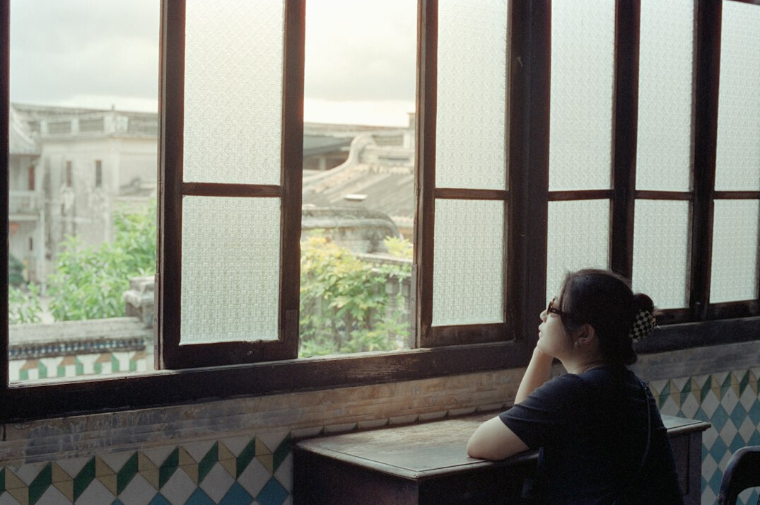 Young Brazilian woman writing thoughtfully in a notebook by a window